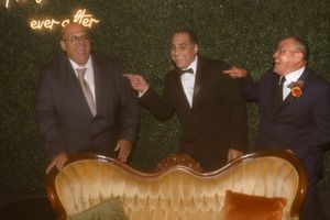 Three men in tuxedos pose humorously behind a vintage gold couch at a formal event.