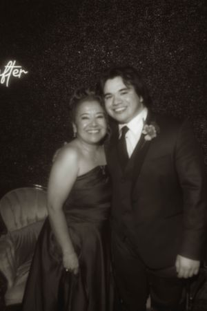 A couple in formal attire pose together at an evening event with a neon sign visible.