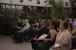 Wedding ceremony audience seated in rows inside a botanical garden setting.