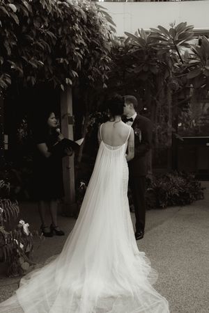Wedding ceremony in a garden conservatory with flowing white bridal gown in focus.
