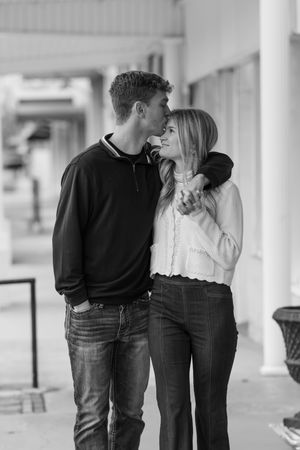 Black and white photo of a couple sharing tender moments along a columned walkway.