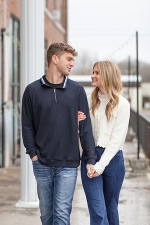 A couple in denim and dark sweaters walking together along a colonnade.
