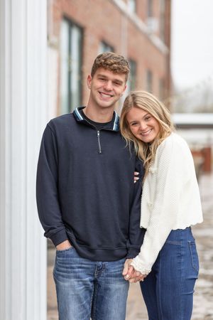 A couple in casual wear smiling and embracing while standing between white columns.