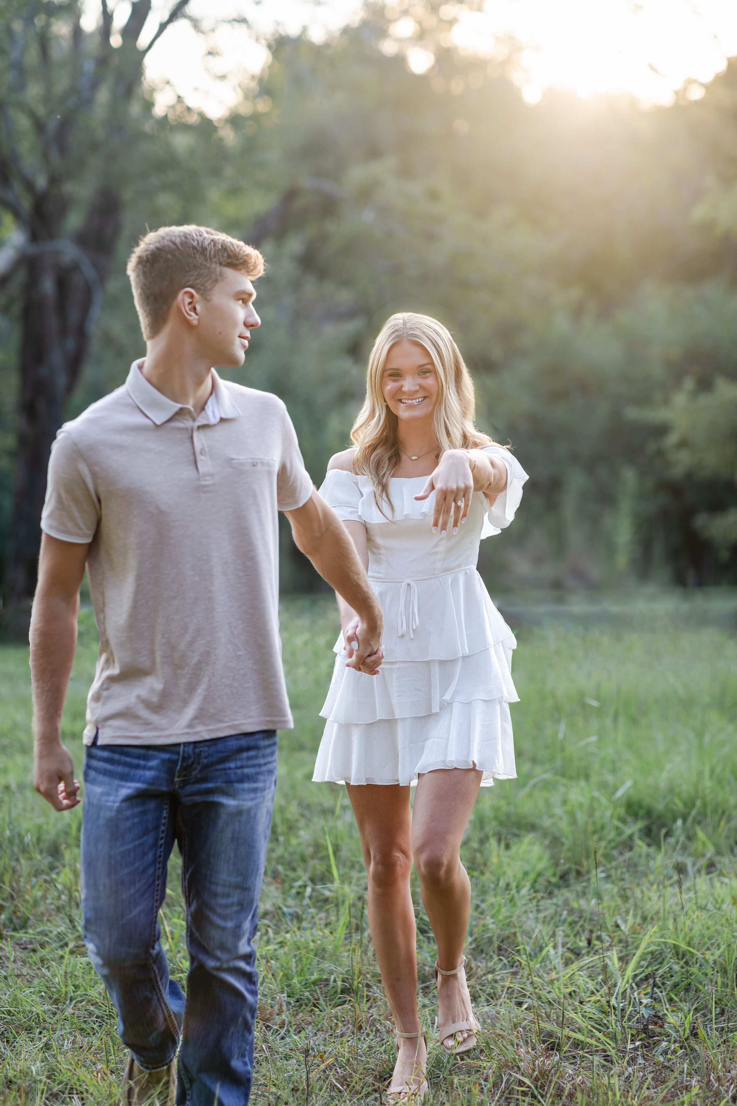 Couple in casual attire walking together through sunlit field at sunset.