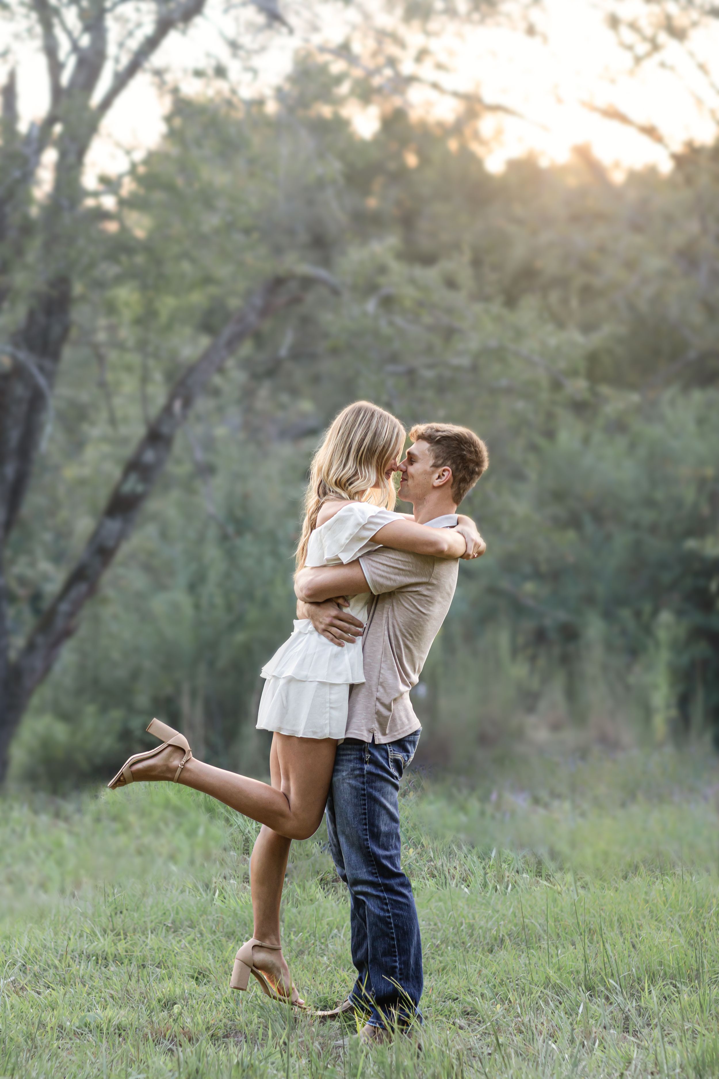Romantic couple embracing in field during golden hour sunset.