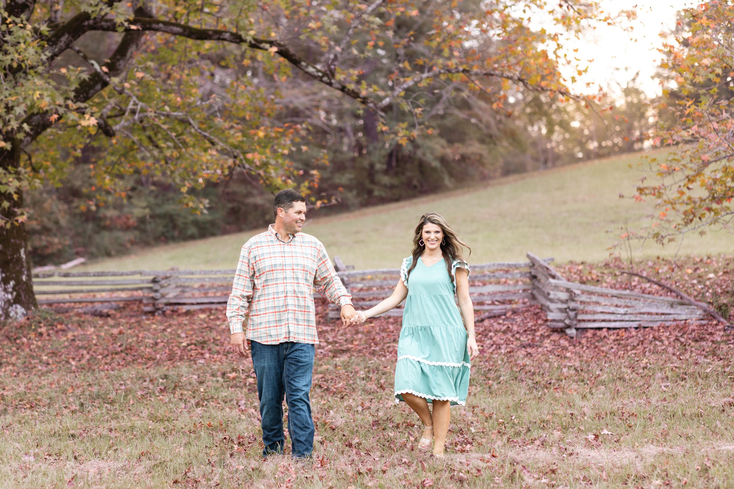 Couple walking through fall foliage with wooden fence in background.