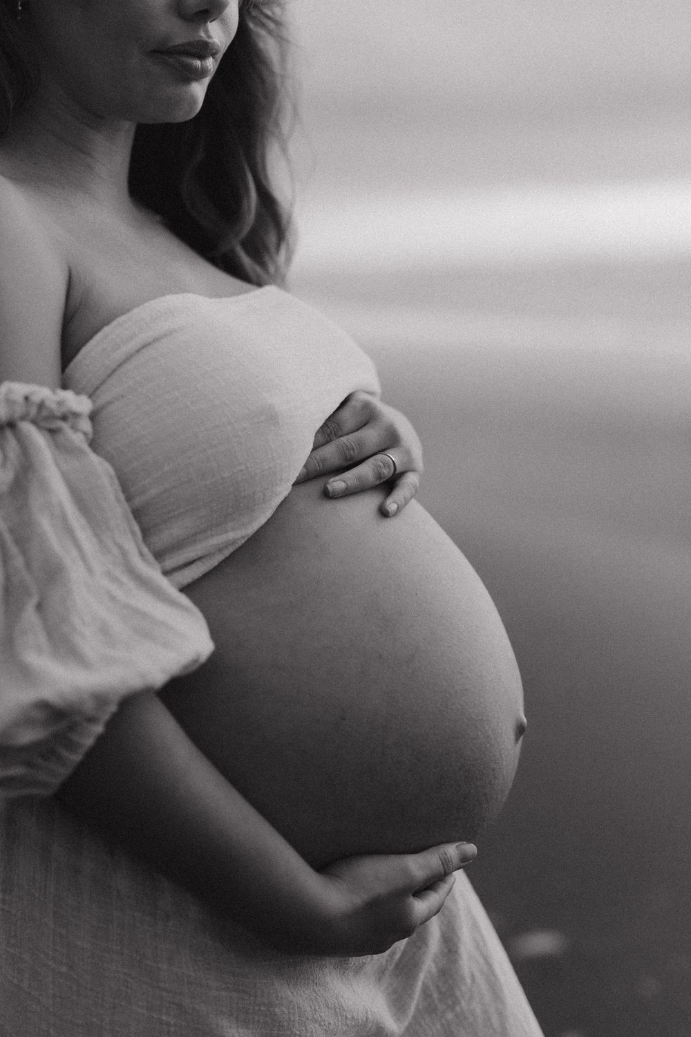 Intimate black and white close-up shots highlighting a pregnant belly with gentle hand placement.