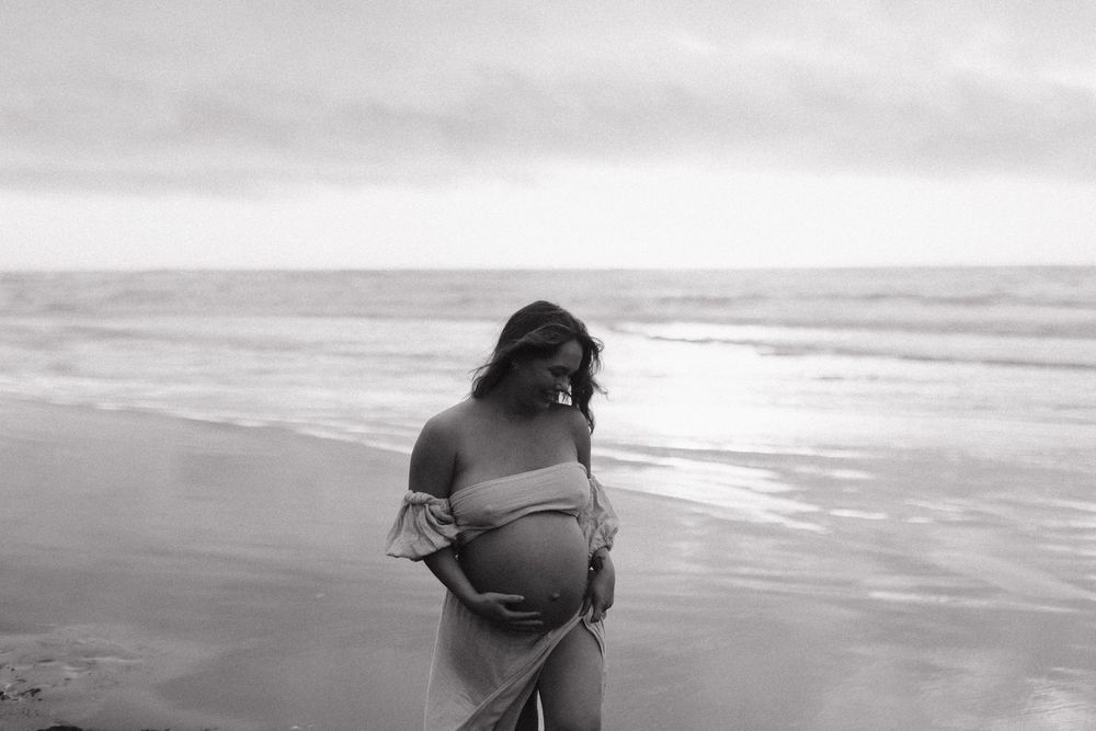 Black and white maternity photograph captured on a misty beach with waves in background.