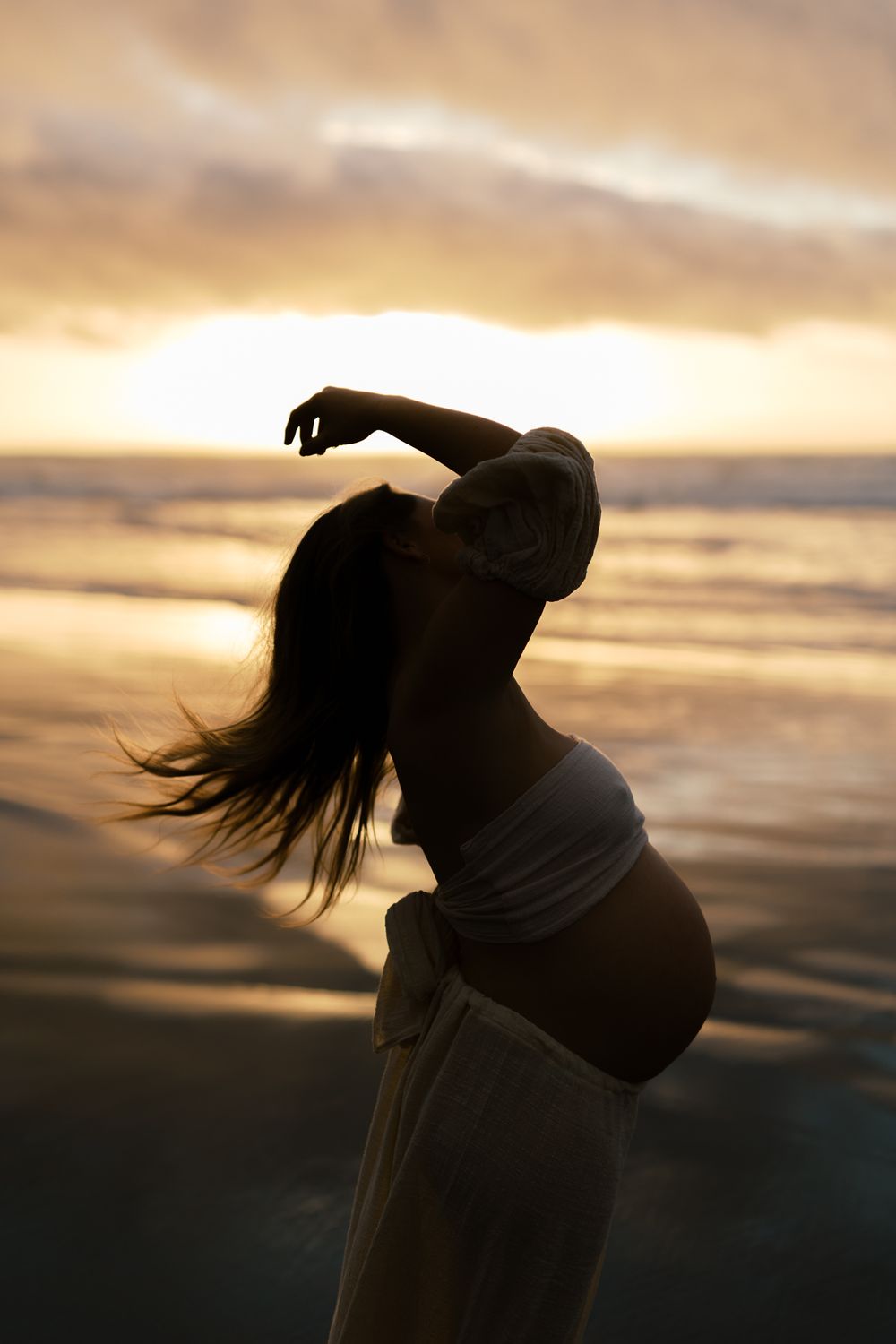 A silhouetted figure dances gracefully against a dramatic sunset sky with flowing hair creating an artistic motion effect.