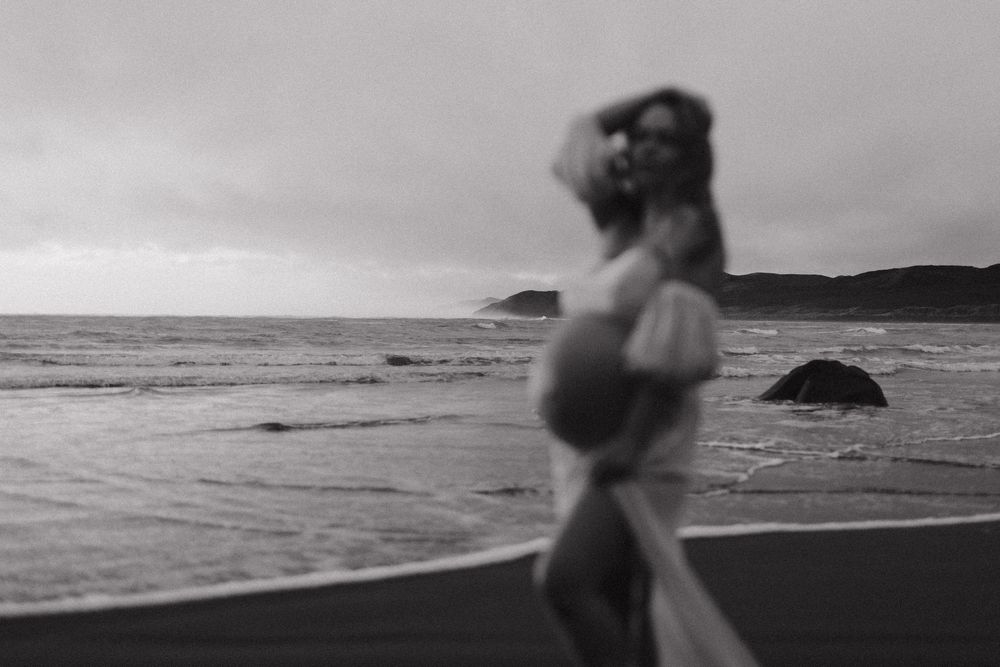 Black and white artistic maternity silhouette against ocean backdrop at dusk.