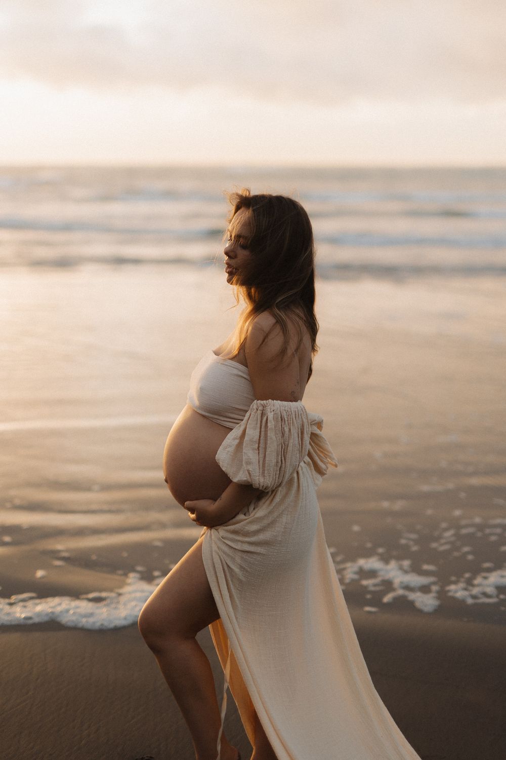 Maternity beach photoshoot with flowing white dress at sunset.