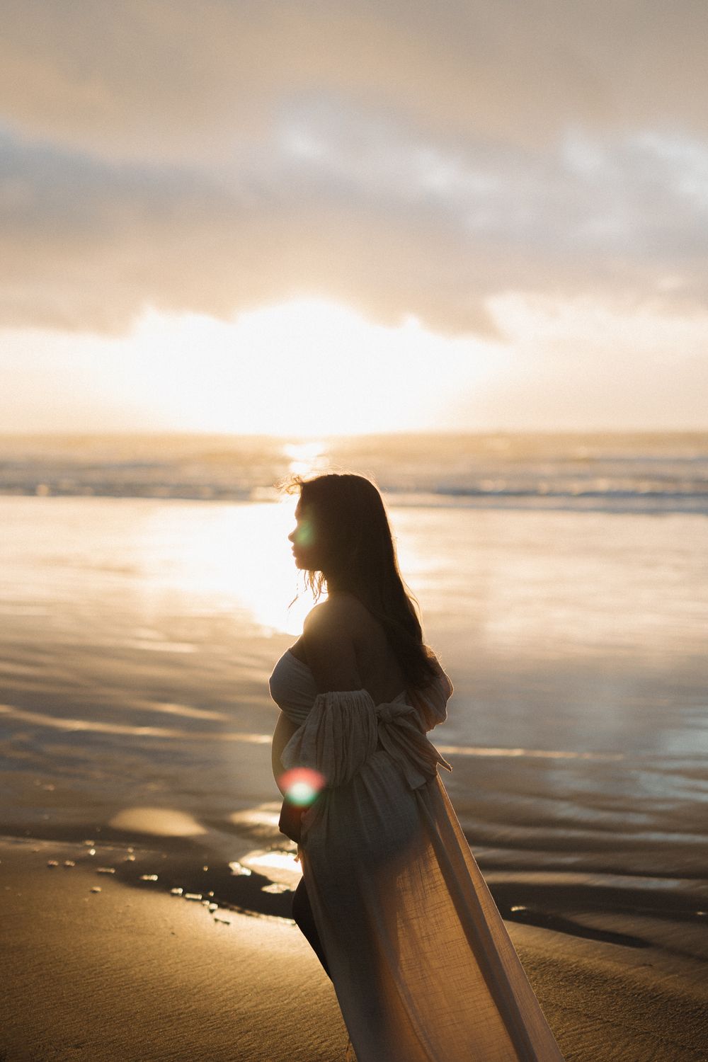 Dreamy silhouette of expectant mother against setting sun on beach.