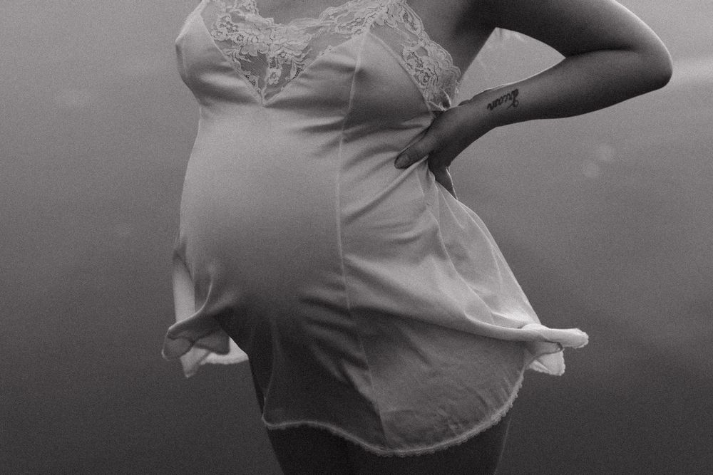 Elegant maternity pose highlighting pregnancy silhouette against dark background.