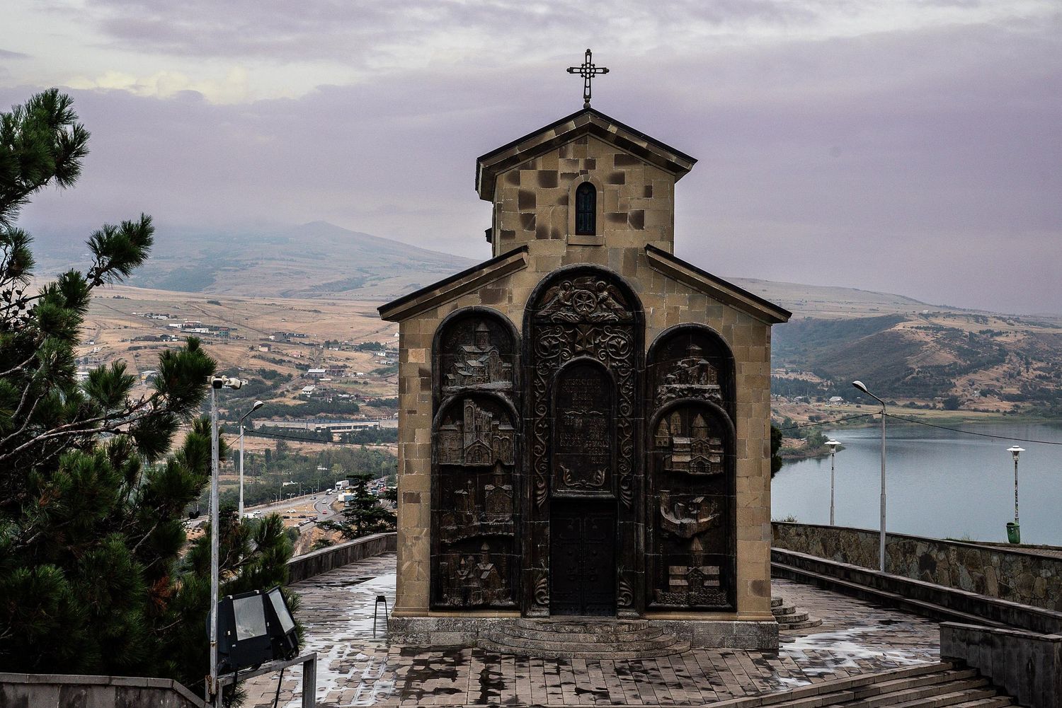 Ancient stone church with cross perched on hilltop overlooking Mediterranean coastal landscape at sunset.