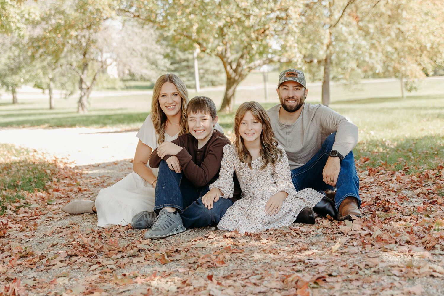 A family group lying together on autumn leaves during an outdoor photo session in a park.