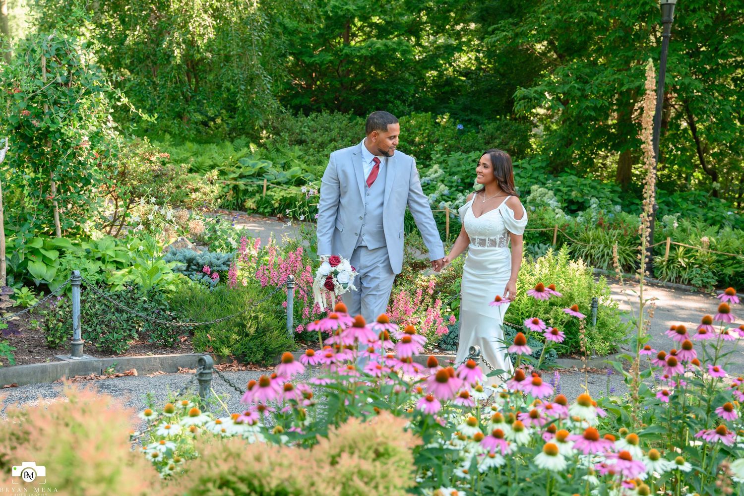 A couple poses together in a lush garden setting surrounded by vibrant pink and white cosmos flowers.