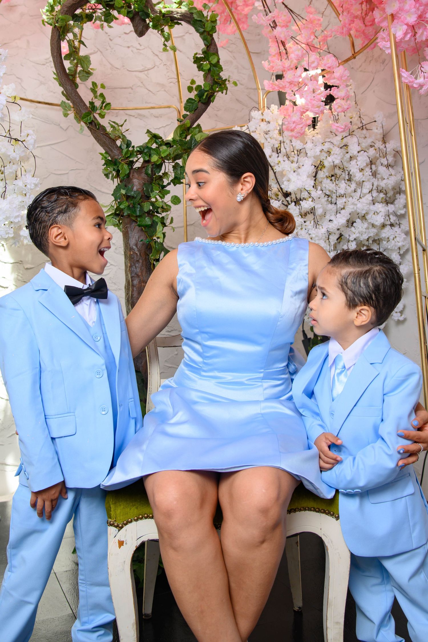 A joyful family moment in matching light blue outfits against a floral backdrop with pink blossoms and greenery.