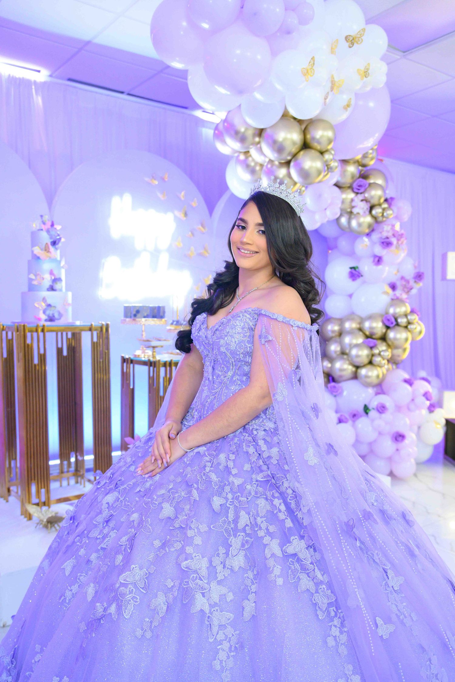 A lavender ballgown with intricate floral embellishments photographed in a luxurious purple-lit room with balloon decor.