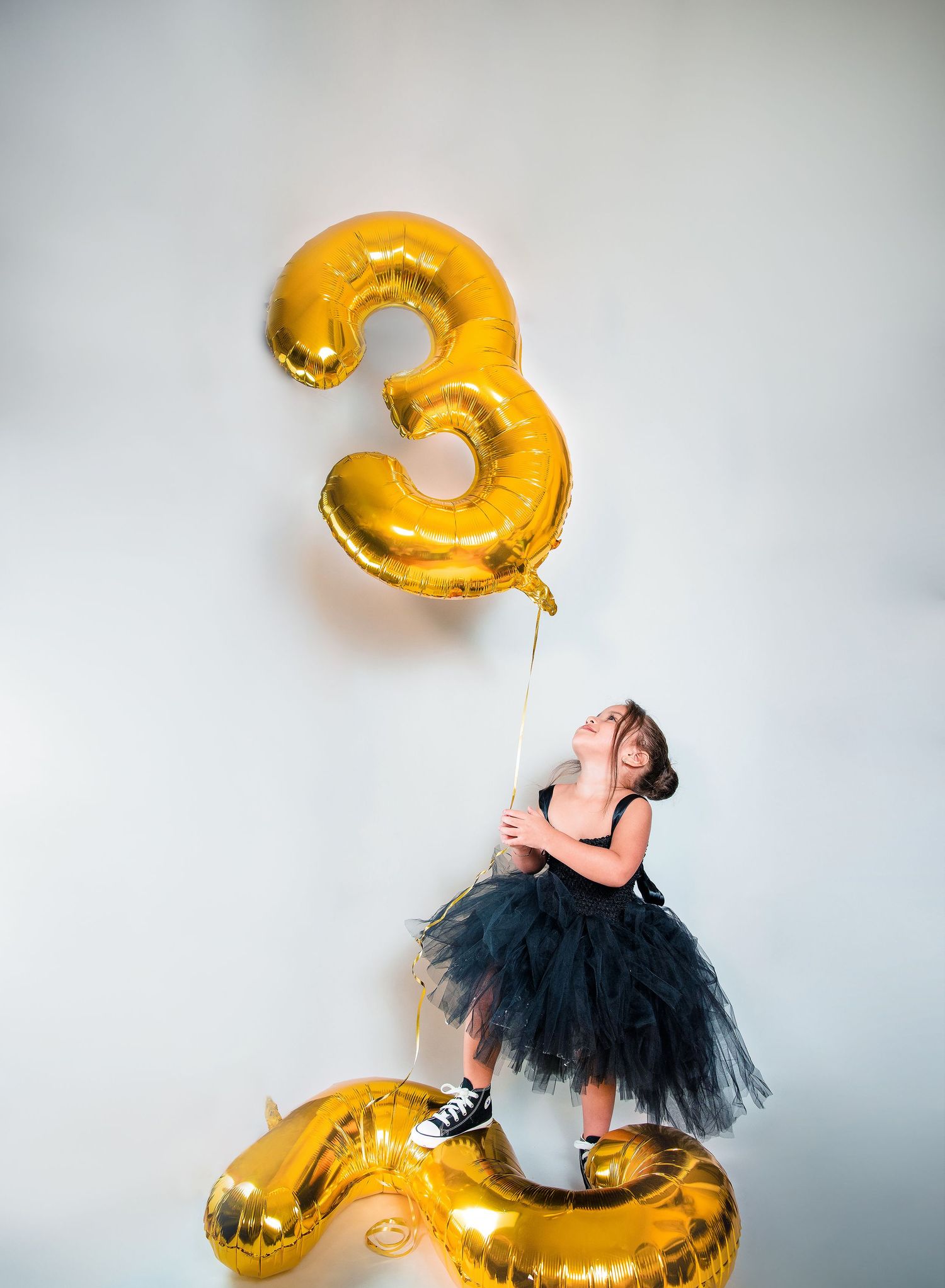 A sequence of photos showing a gold number 3 balloon floating against a white background with a black tutu skirt.