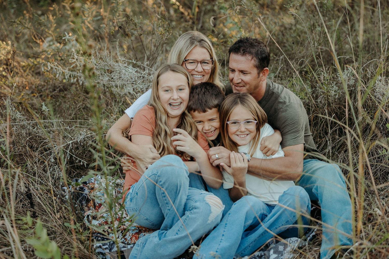 Family wearing denim and white sits together on grass during outdoor autumn photoshoot.