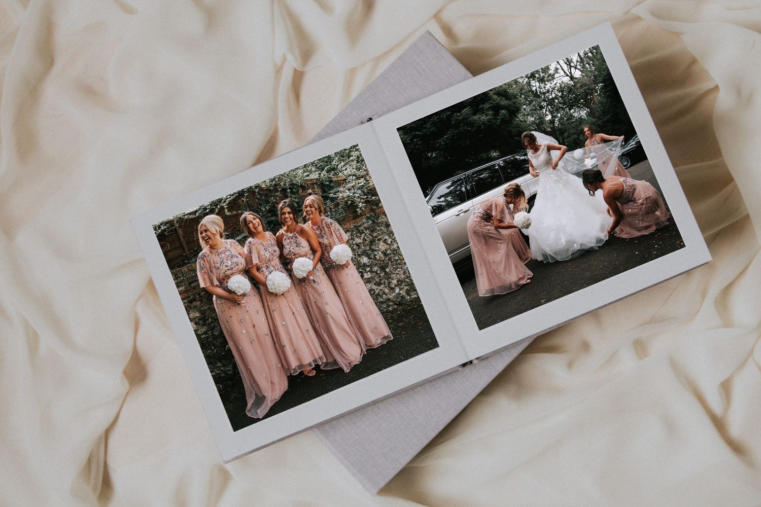 Wedding photo album displaying bridesmaids in pink dresses and a bride with her wedding party on fabric background.