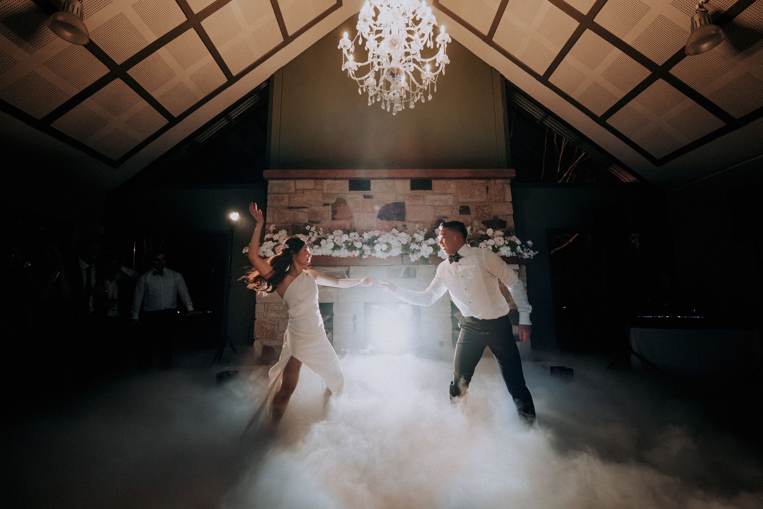 Elegant wedding reception dance floor with chandelier and atmospheric fog effects.