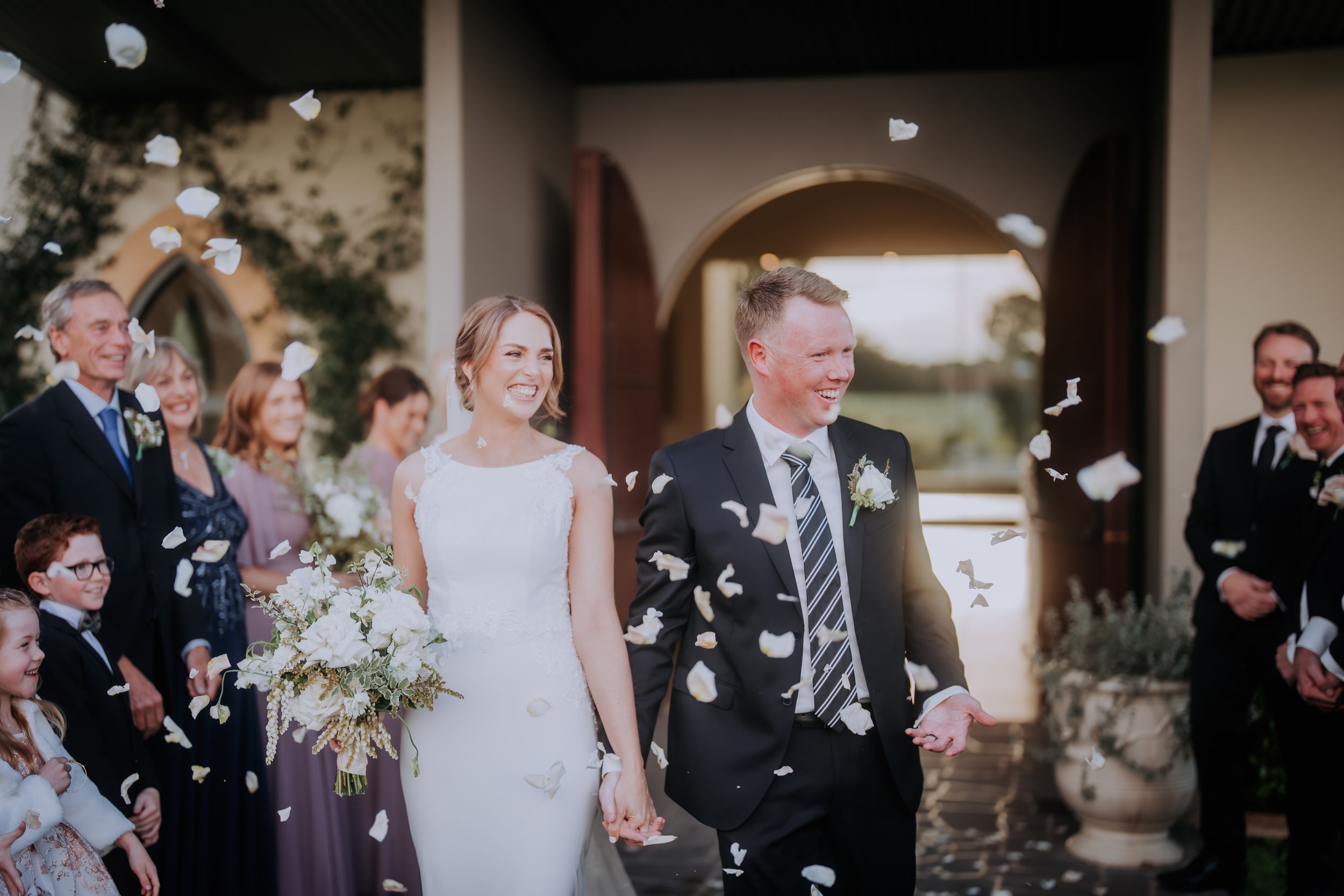 Wedding celebration with guests throwing confetti as couple walks through outdoor venue.