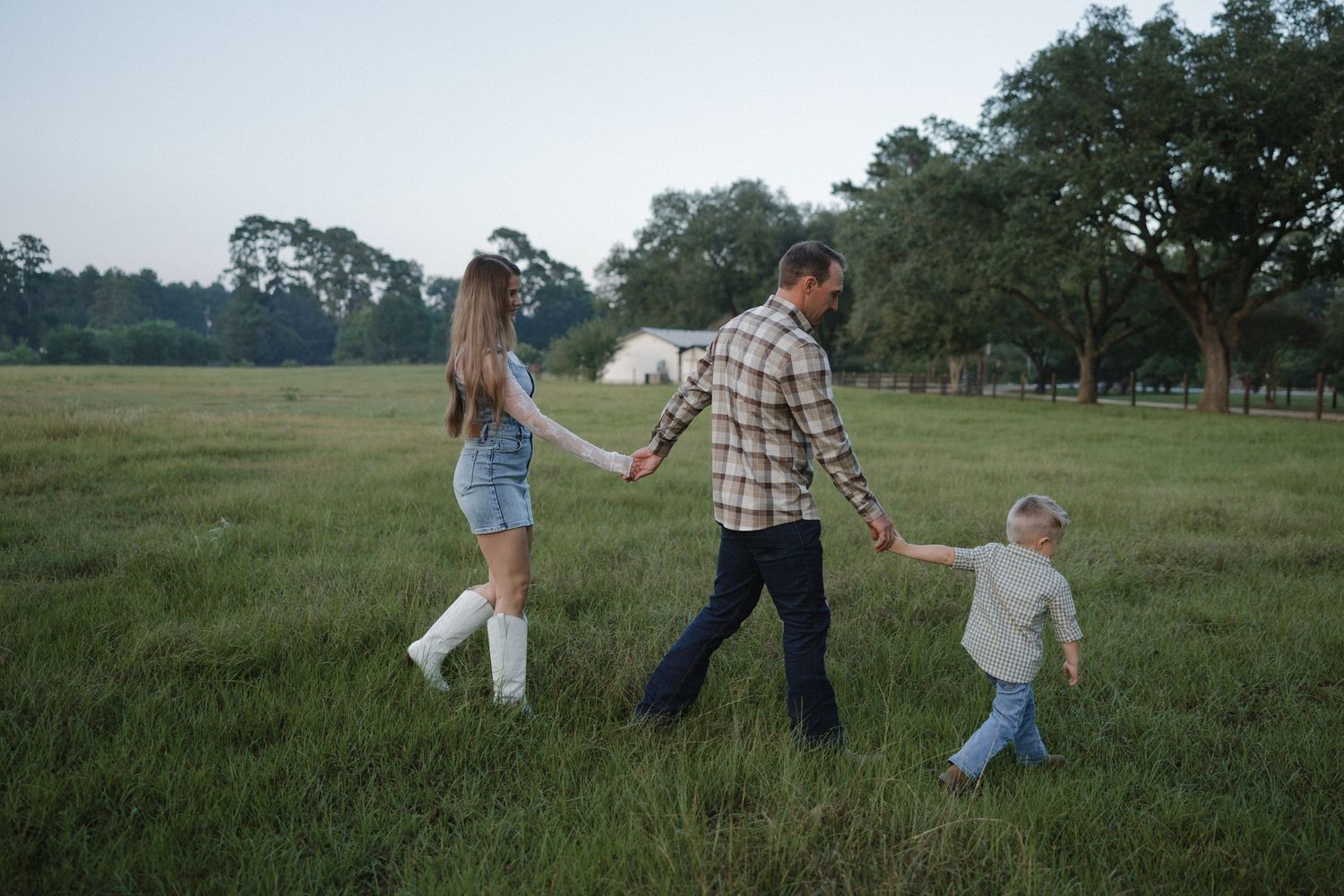 A couple playfully runs and dances together in a scenic green field at sunset.