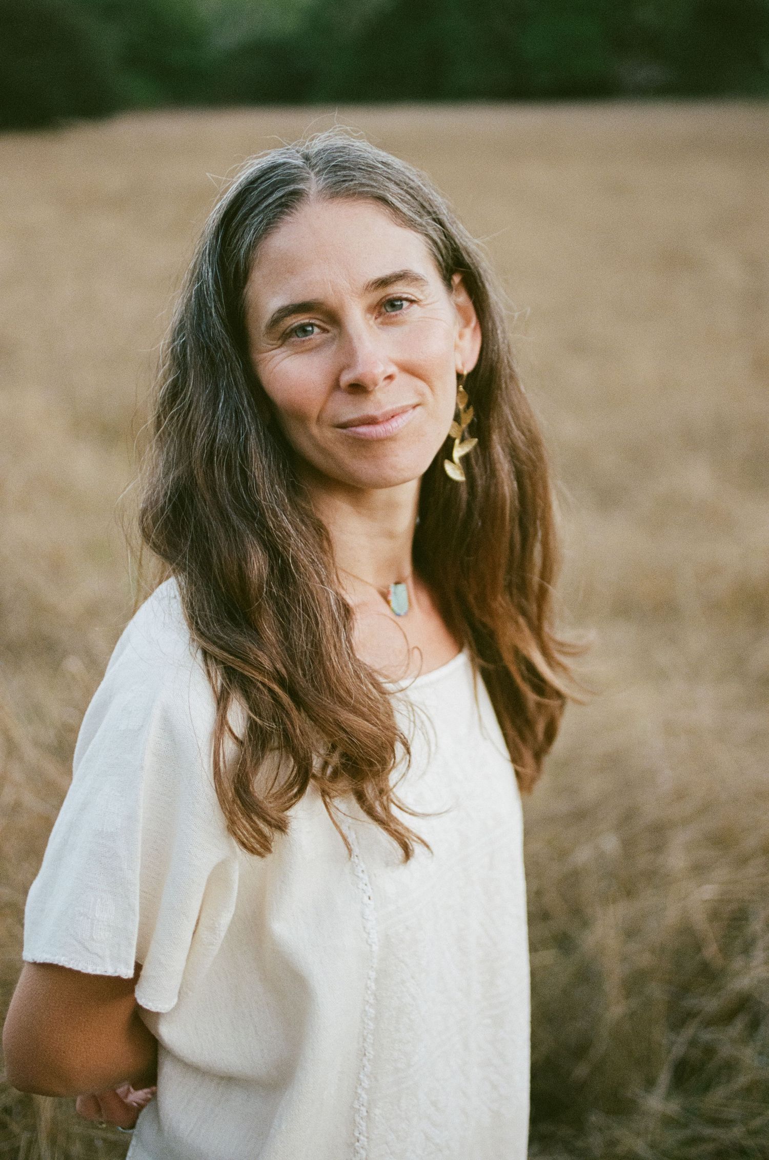 Portrait of person in white top standing in golden field during sunset.