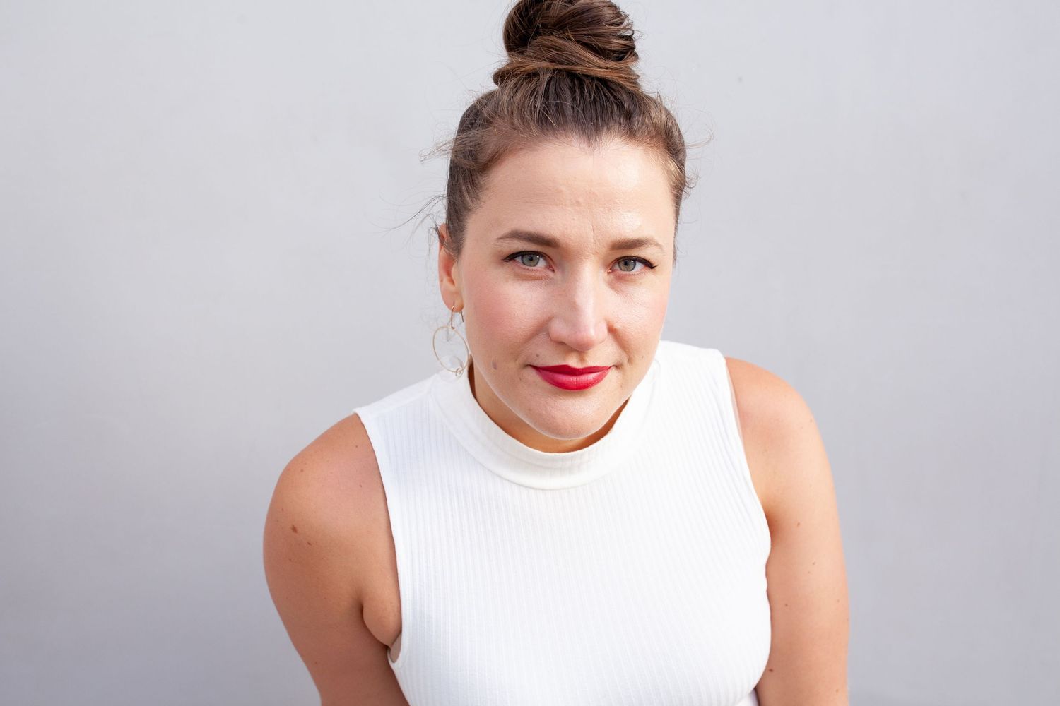 Minimalist studio portrait in white sleeveless top against light background.