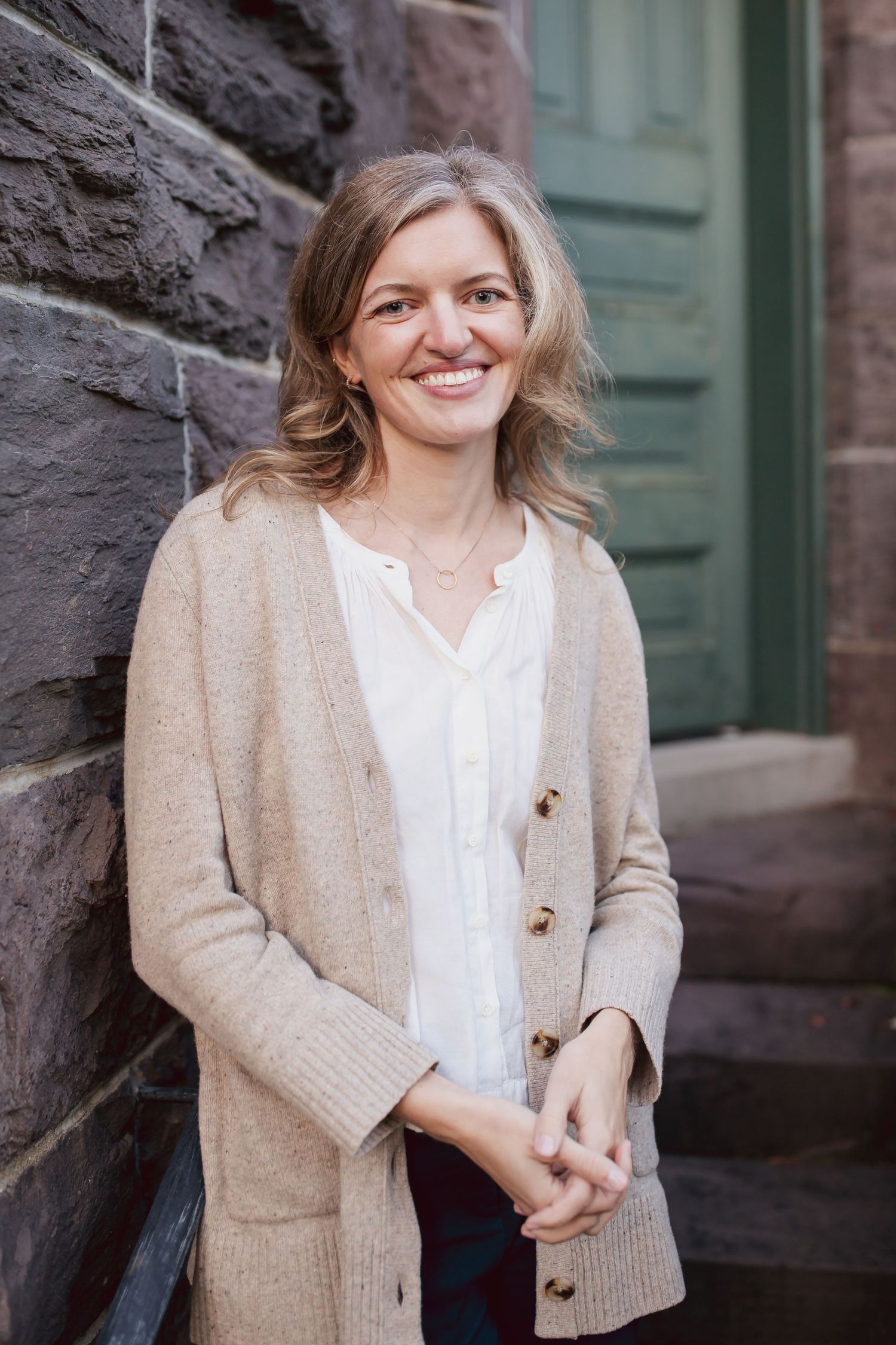 Casual portrait against stone wall wearing beige cardigan and white button-up shirt.