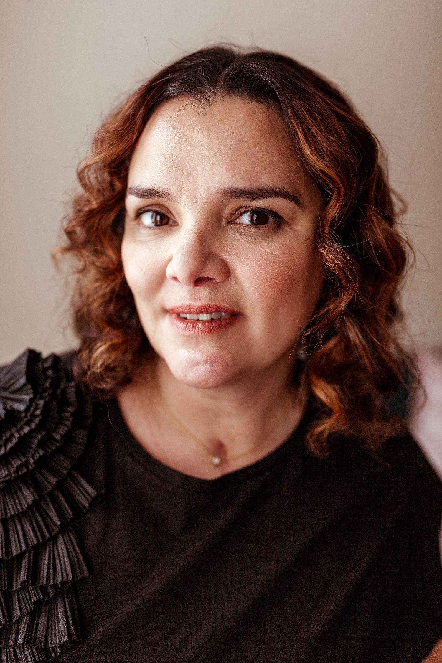 Portrait of person with curly brown hair wearing black top with ruffled detail.