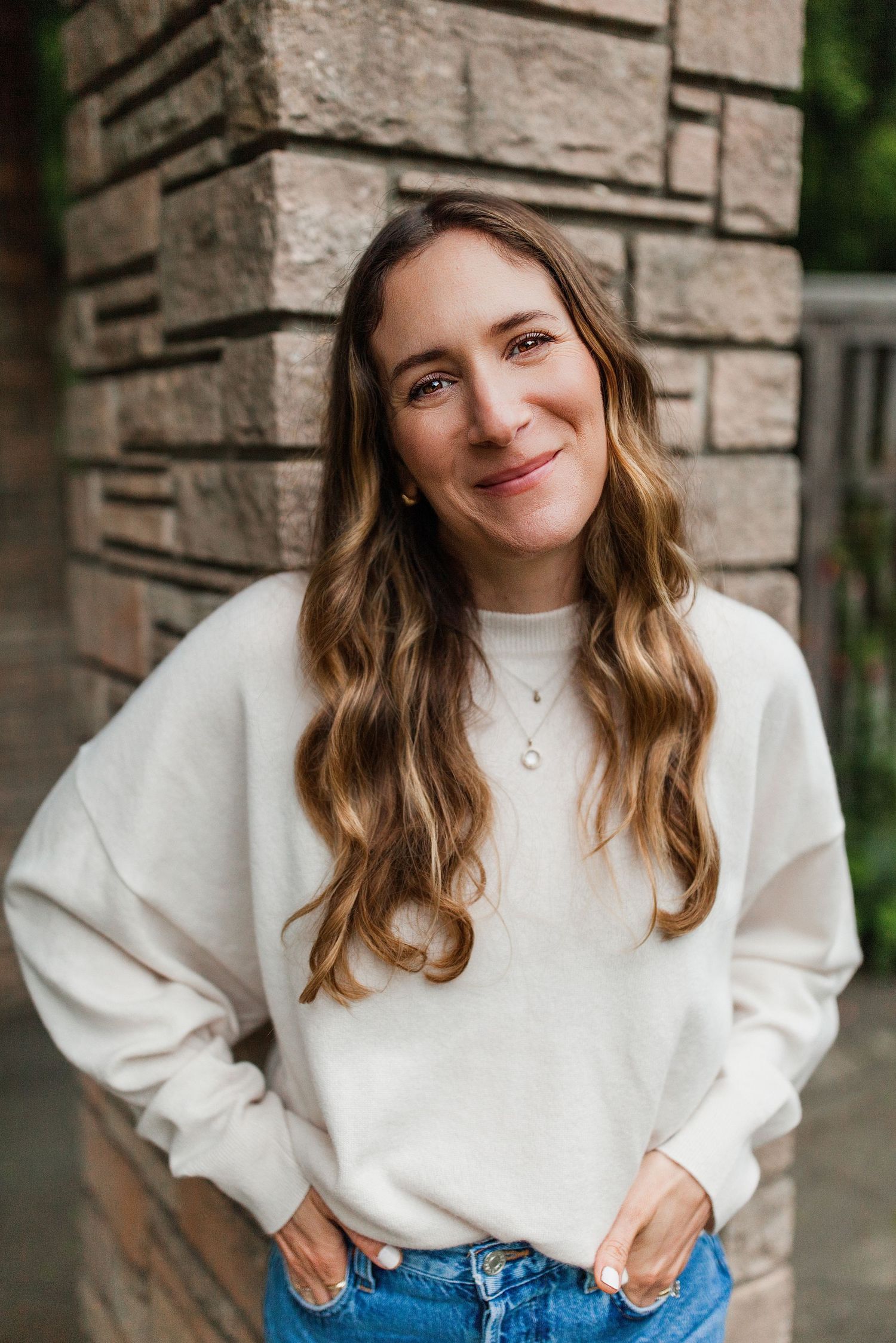 Lifestyle portraits against a stone wall backdrop showcasing a cozy white sweater and denim outfit.