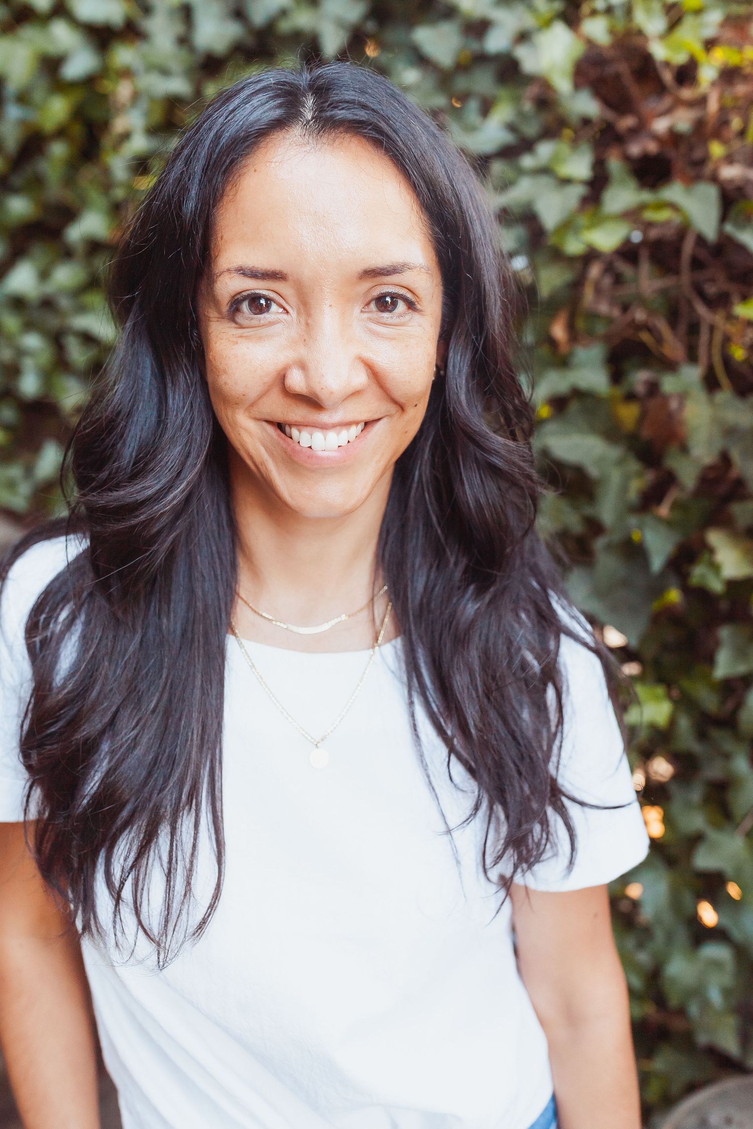 Natural outdoor portrait with dark hair and white t-shirt against ivy background.