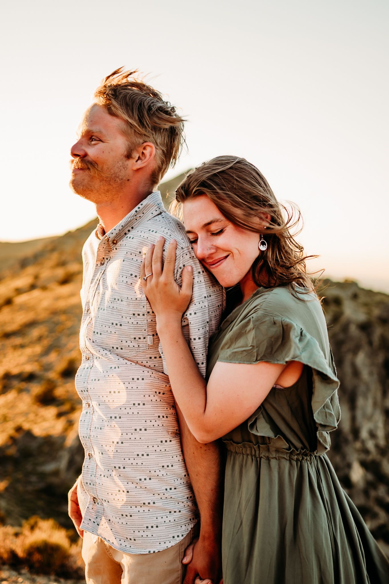 A romantic couple embraces at sunset against a mountainous backdrop.