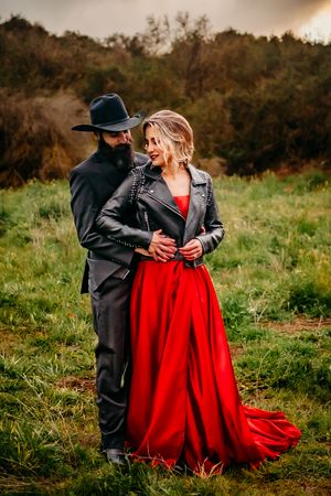 Couple in contrasting black and red attire share an intimate moment in a grassy field.