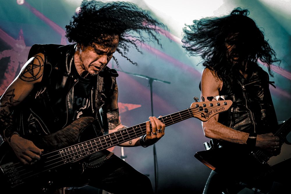 Bass guitarist plays instrument with dynamic movement captured in teal stage lighting.