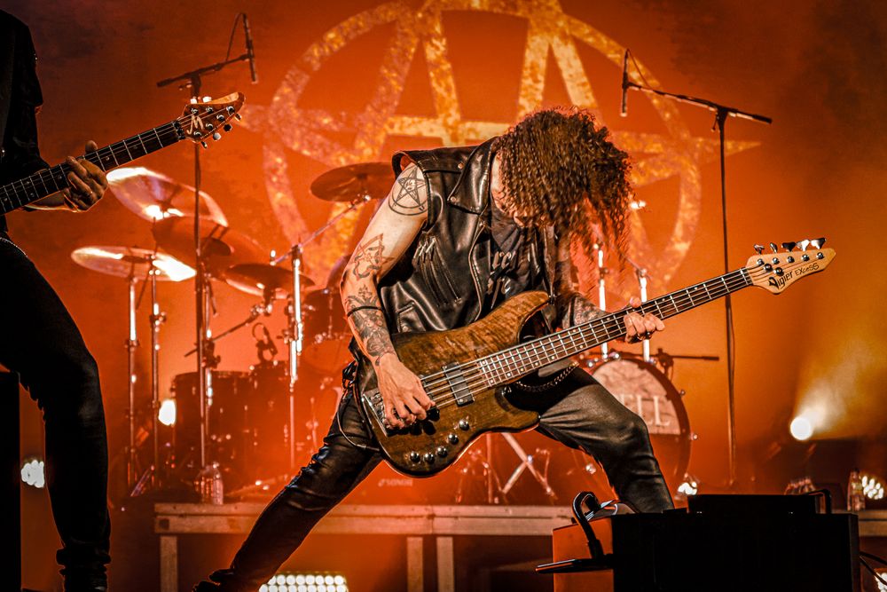 Band members perform with guitars under warm orange stage lighting during rock concert.