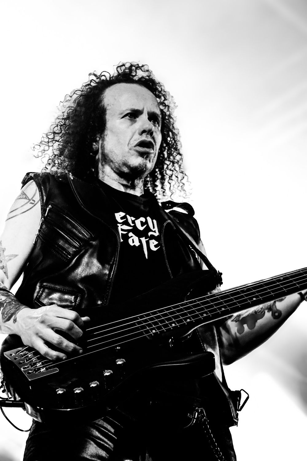 Bass guitarist in leather jacket plays instrument against black and white background.