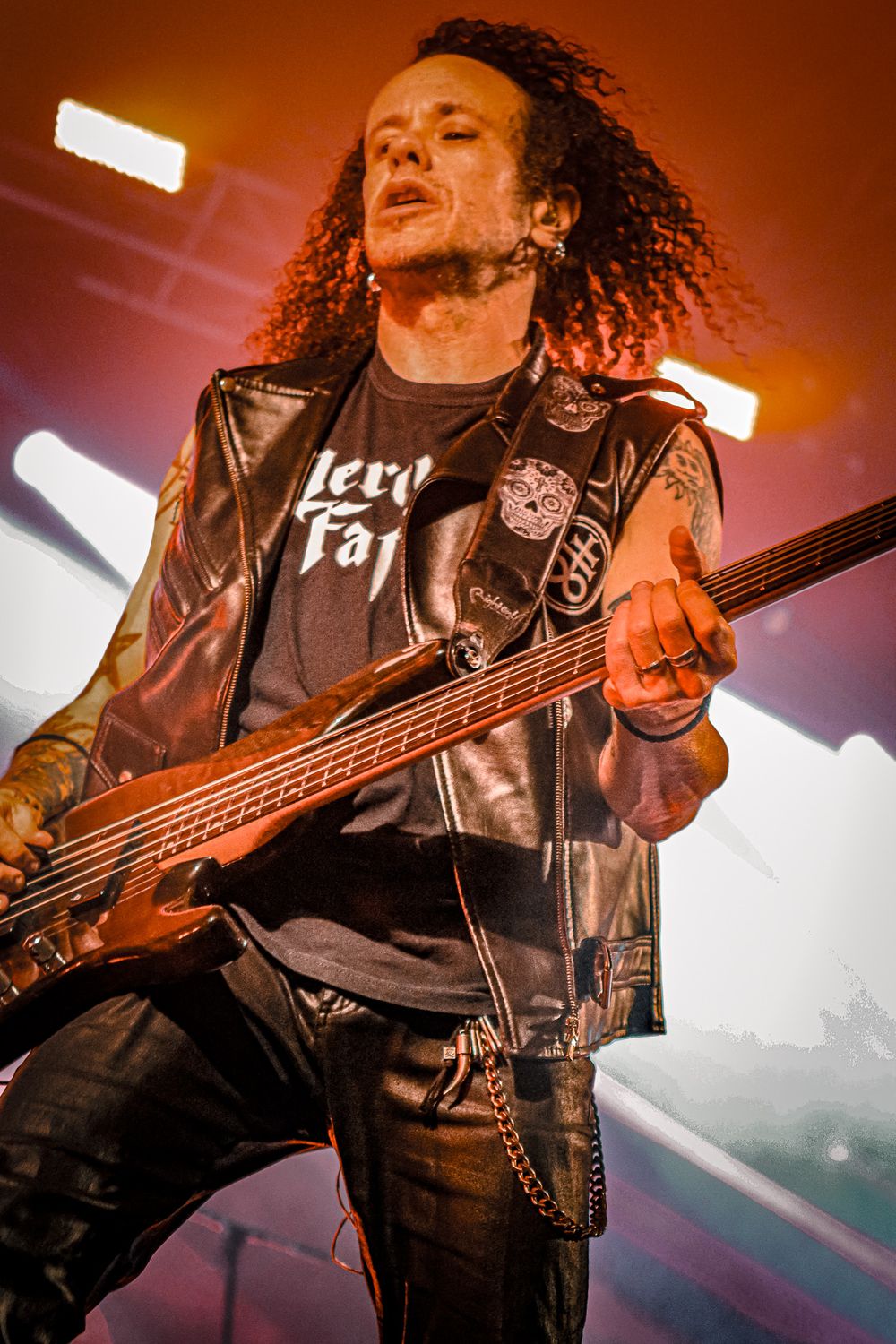 Bass player performs with curly hair and leather jacket under warm stage lighting.