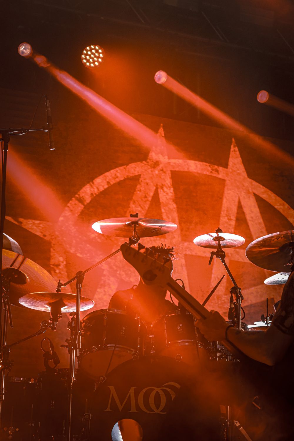 Drum kit setup on stage illuminated by dramatic red lighting and spotlights during a live performance.