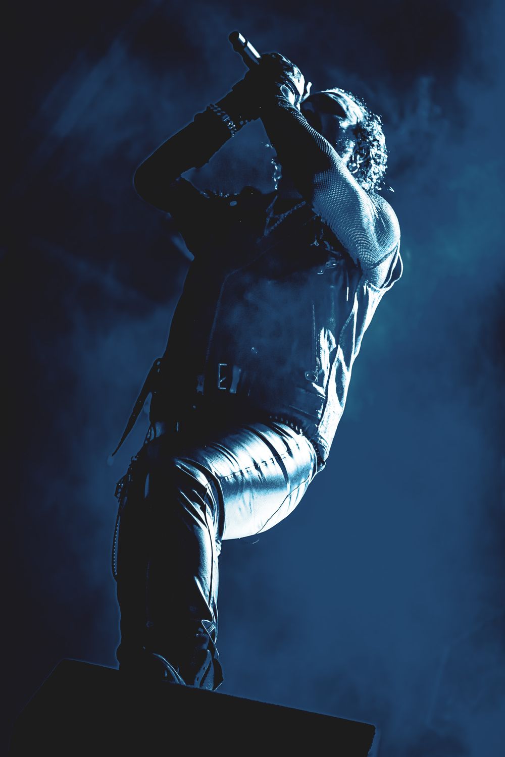 Dramatic silhouette of performer on stage with blue atmospheric lighting and fog effects.