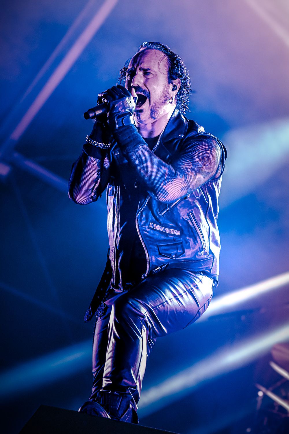 Concert performer sings passionately on stage with dramatic blue lighting and theatrical atmosphere.