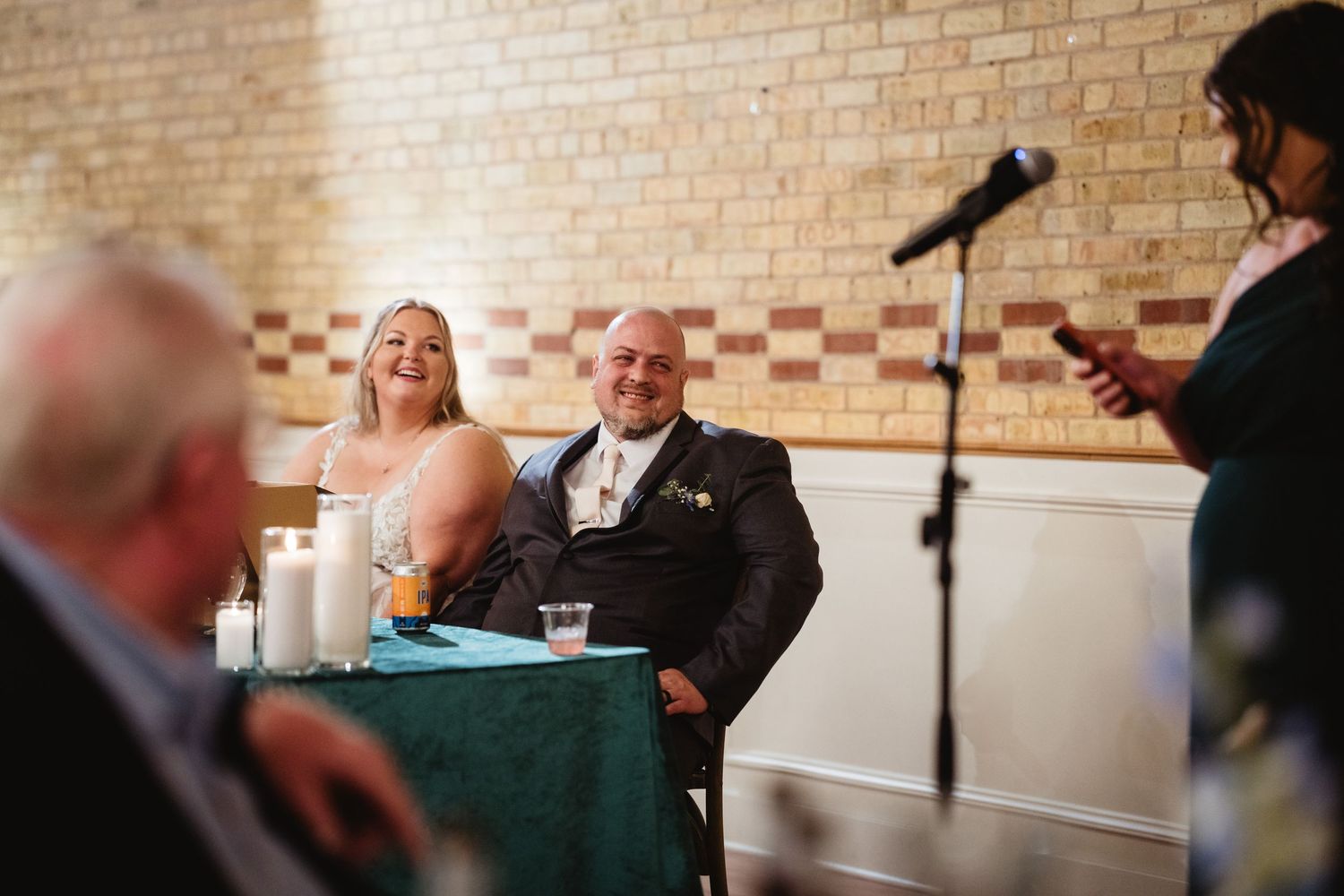 Wedding reception in a rustic brick-walled venue with guests seated at long tables.