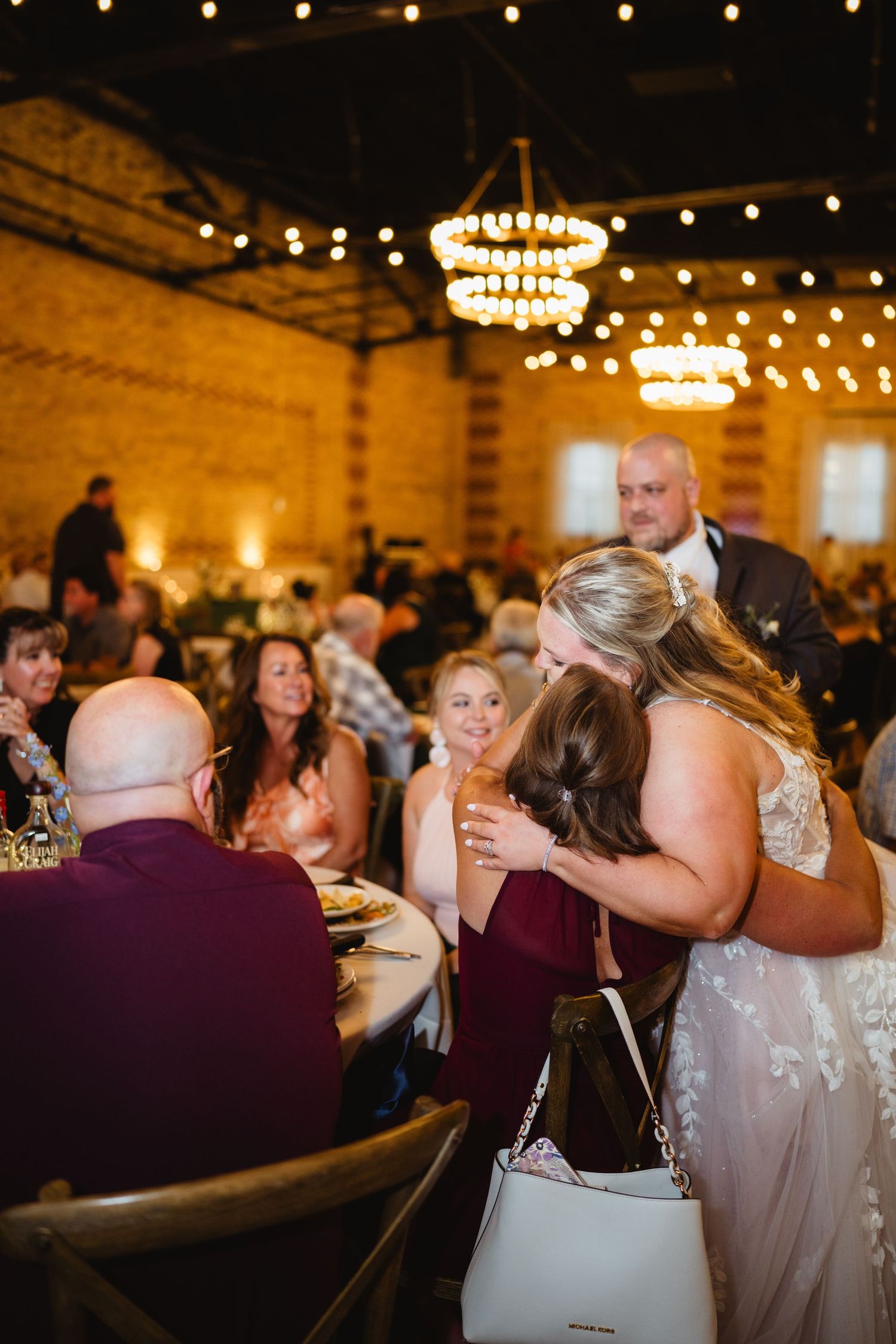 Wedding reception guests dance together under warm lighting and string lights in a rustic venue.