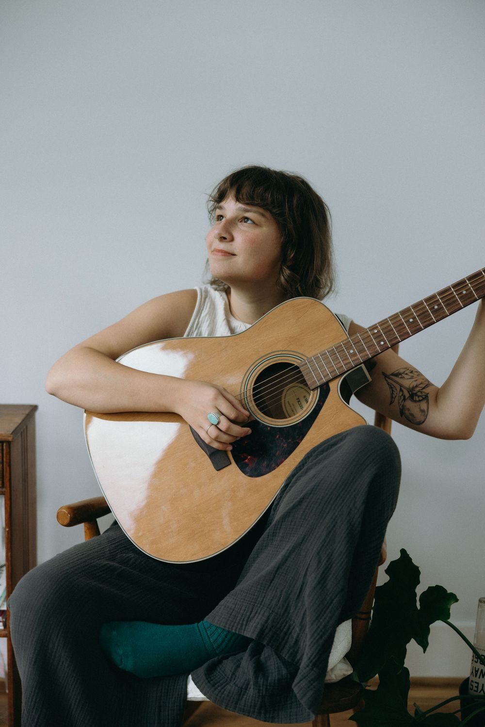 A musician in black clothing holds an acoustic guitar while seated in a series of artistic poses against a light background.