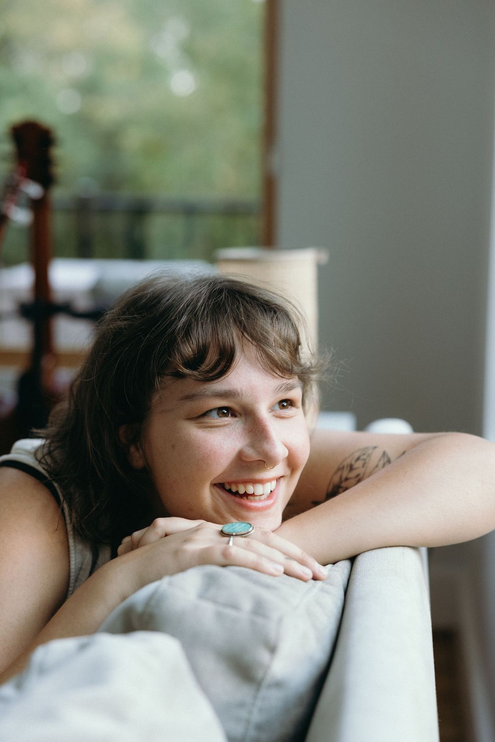 Someone rests their head on a white couch cushion while smiling brightly near a window.