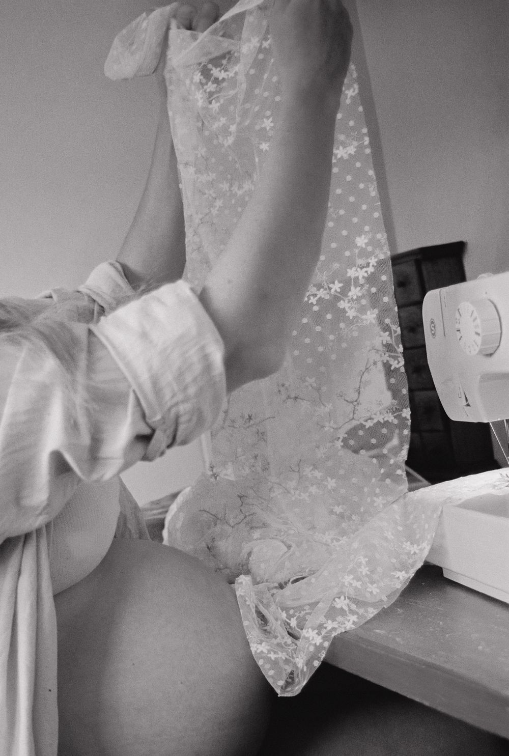 Black and white image showing close-up details of a lace wedding dress being fitted and adjusted.