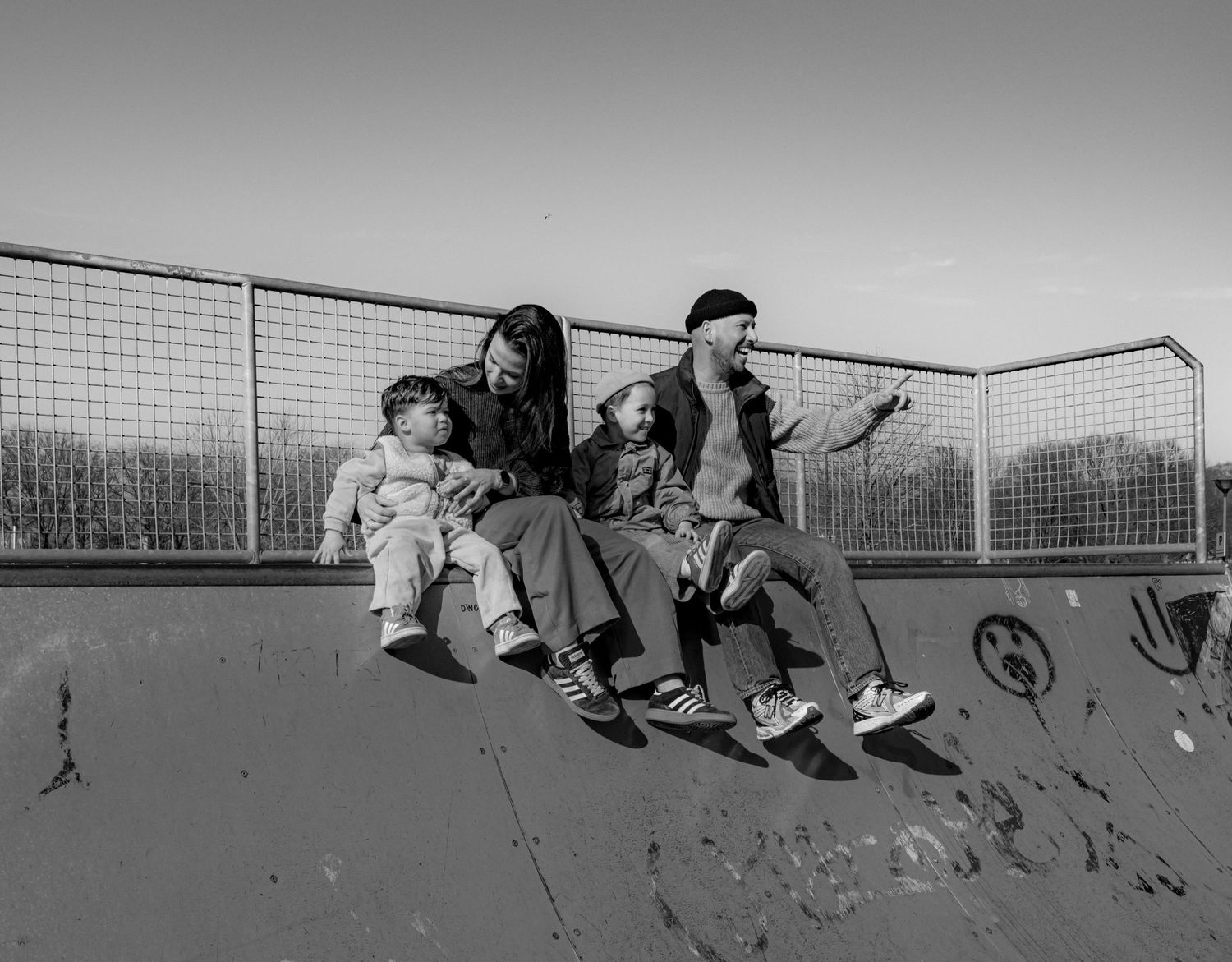Silhouettes of people sitting on a fence against a grey sky.
