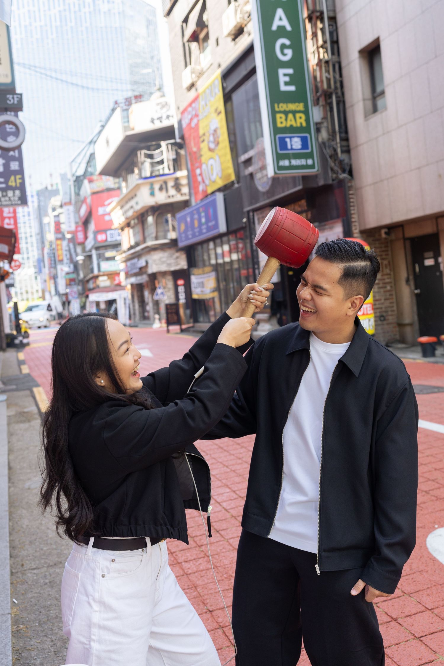 A couple shares a playful moment drinking from red cups on a city street.